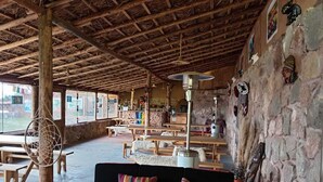 A rustic interior with wooden benches and tables, a black sofa with colorful cushions, and a stone wall with various decorations. - Pachamama Hampina Wasi Centro Ancestral - All Inclusive (Maras)