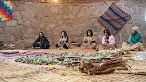 A group of people sitting on a woven floor in a stone-walled room with blankets and flowers. - Pachamama Hampina Wasi Centro Ancestral - All Inclusive (Maras)