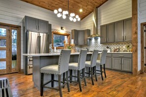 A modern kitchen with grey cabinets, a central island with bar stools, a large window, and a wooden ceiling. - A Great Escape - Modern Cabin w/ views & waterfall (Blue Ridge)
