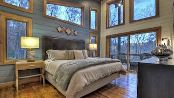 Un dormitorio con una cama grande, cabecera de madera, varias ventanas y vistas a árboles.