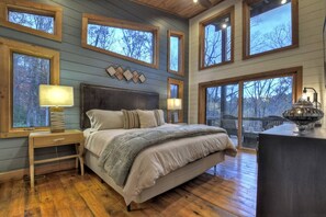A bedroom with a large bed, wooden headboard, multiple windows, and a view of trees. - A Great Escape - Modern Cabin w/ views & waterfall (Blue Ridge)