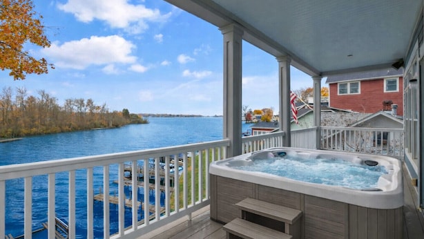 Ein Whirlpool auf einer Holzterrasse mit Blick auf einen See und Häuser im Hintergrund.