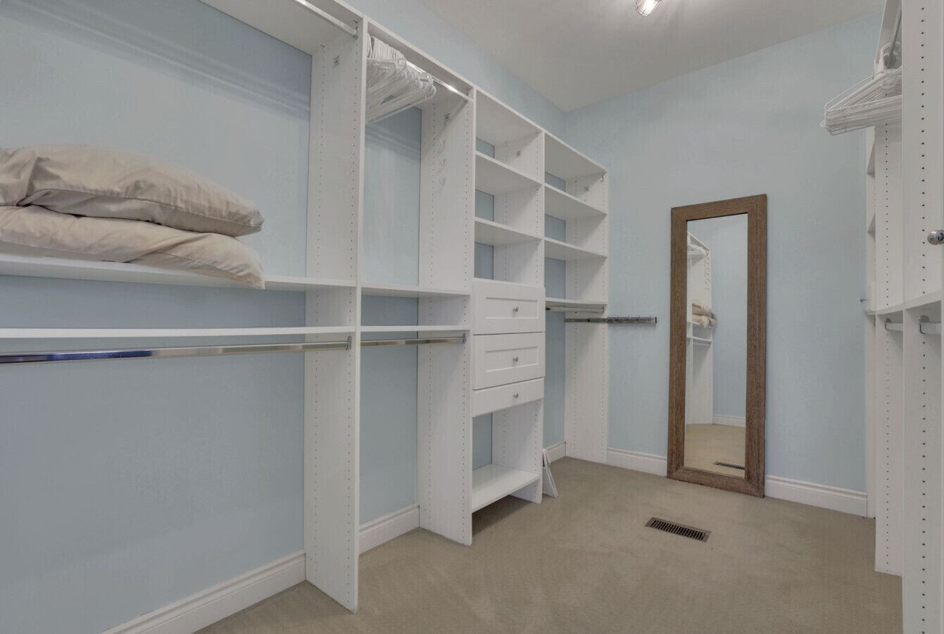 A walk-in closet with open shelving, a mirror, and a hanging rod.