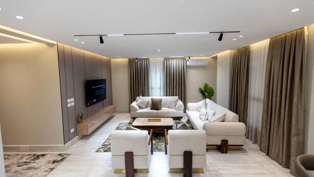 A modern living room with a sofa set, a coffee table, and a flat-screen TV mounted on the wall. - 3-bedroom apartment in enchanting Cairo Governorate with AC (Cairo Governorate)