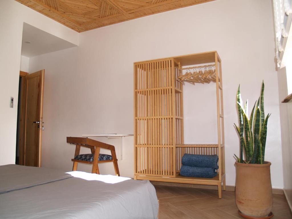 A bedroom with a bed, a wooden chair, a hanging chair, and a potted plant.