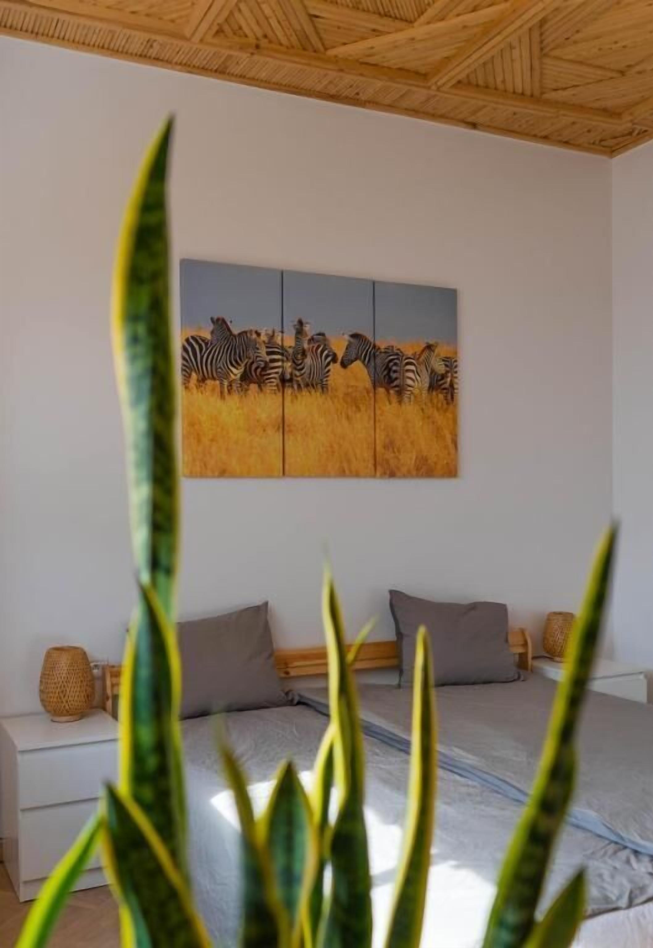 A bedroom with a bed, pillows, a bedside table, and a painting of zebras on the wall.