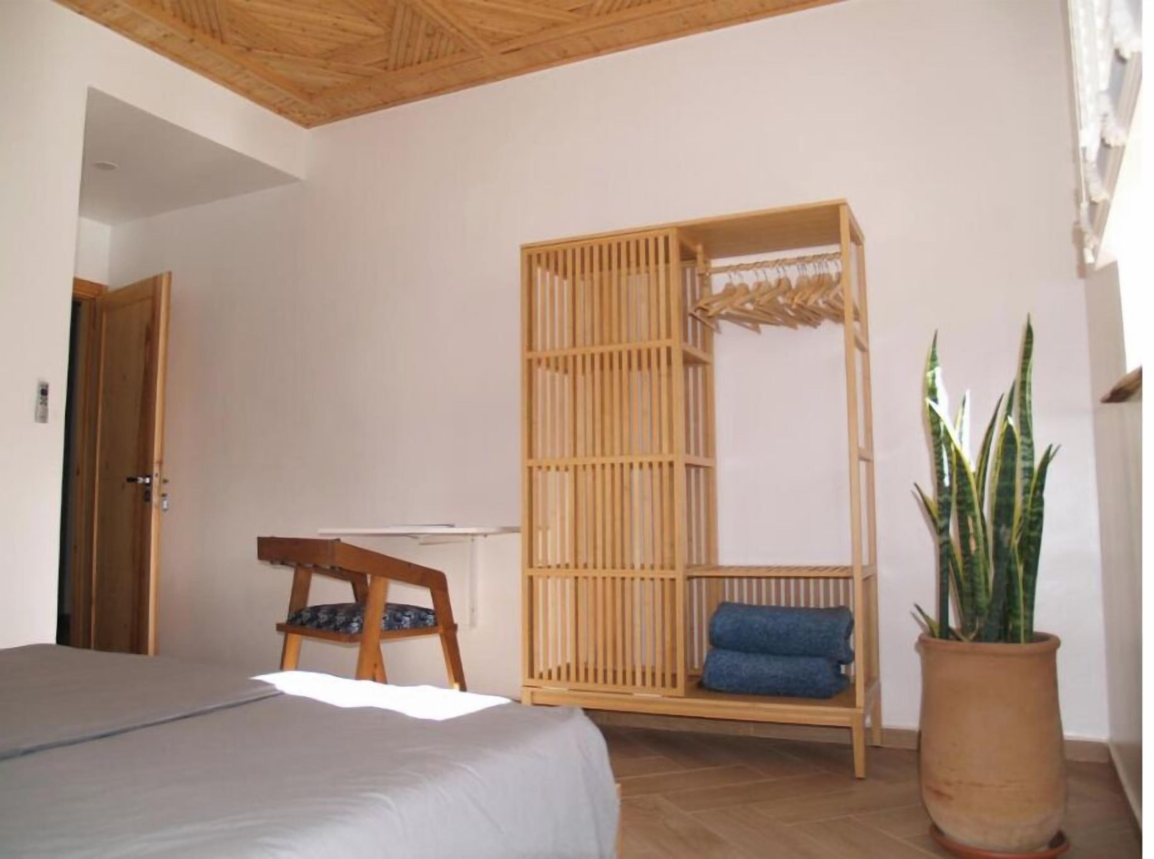 A bedroom with a bed, a wooden crib, a chair, and a potted plant.