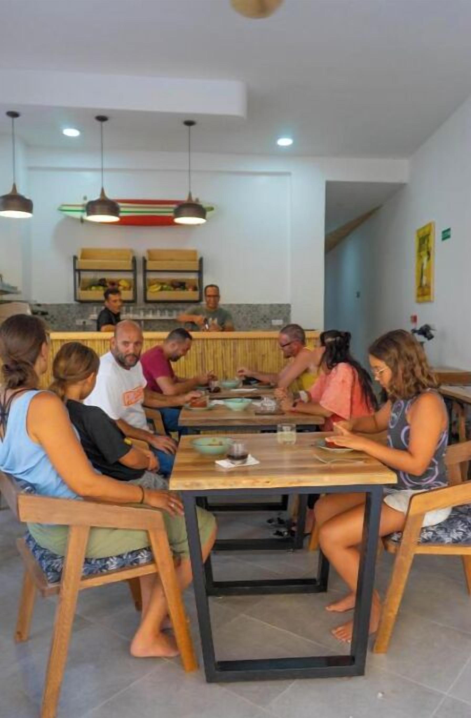 A group of people dining at a wooden table in a modern restaurant with pendant lighting.