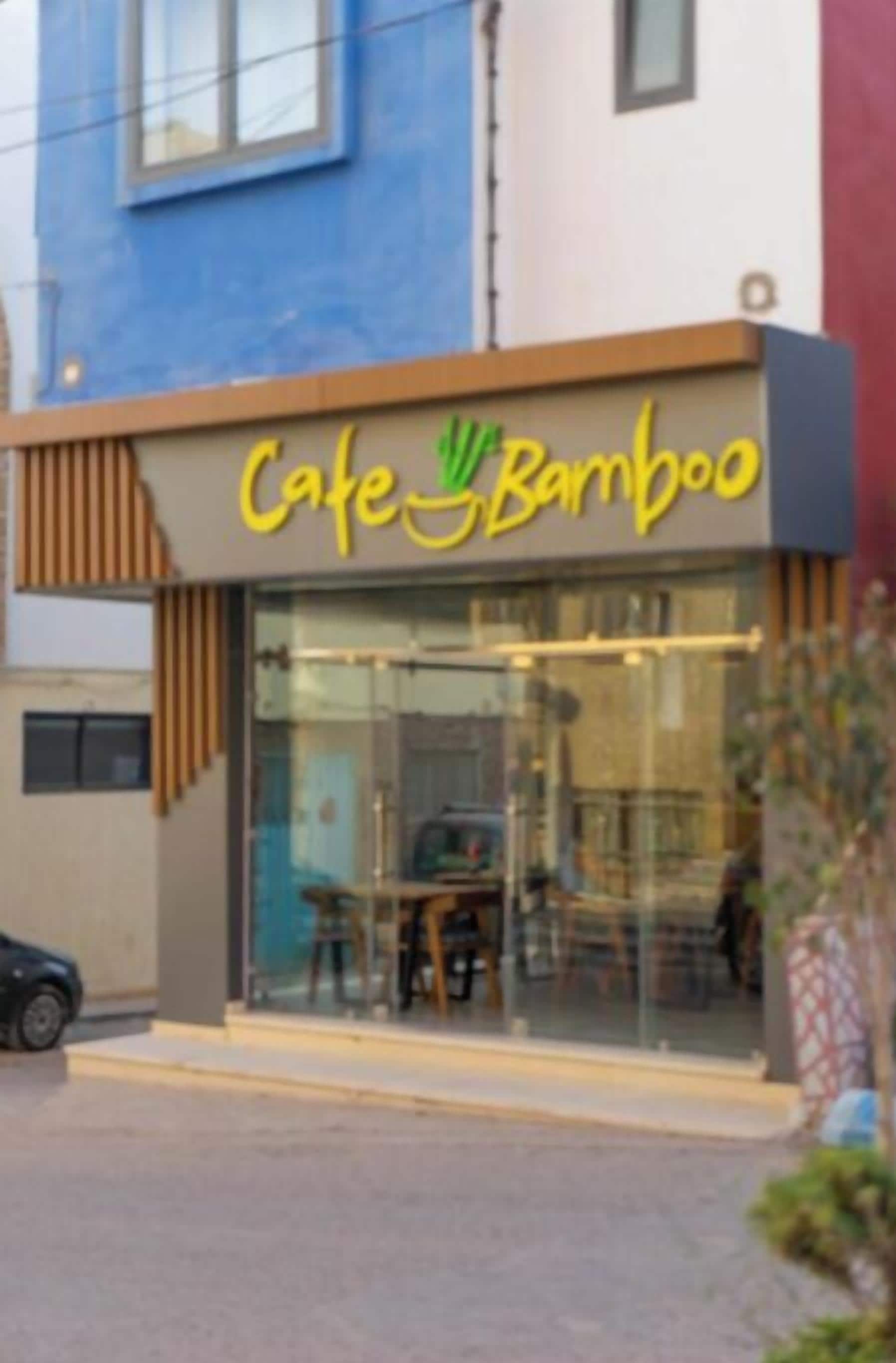 A cafe named 'Cafe Bamboo' with a modern design, featuring a glass facade and outdoor seating visible through the windows.