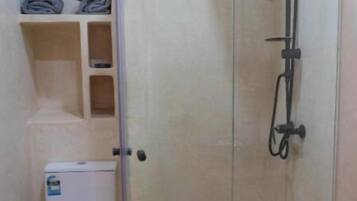 Un baño pequeño con inodoro, ducha con cerramiento de vidrio y repisas con toallas dobladas.