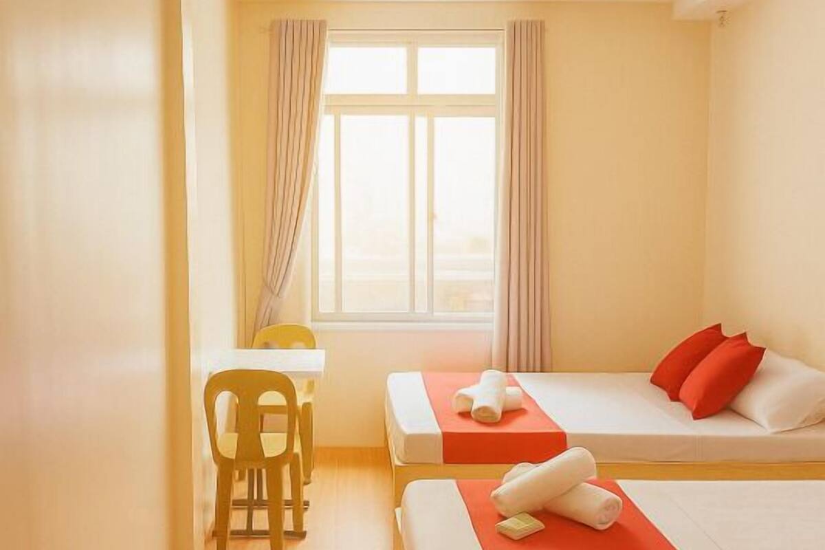 A hotel room with two beds, a small table, and a chair.