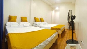 A hotel room with two beds, each with white bedding and yellow accents, a standing fan, and a small white laundry basket. - Baden Powell Hostel  (Baguio)