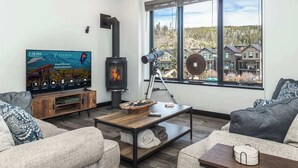 Una sala de estar con un televisor de pantalla plana grande, una chimenea de leña y vistas a una zona residencial a través de un ventanal amplio.
