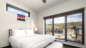 Un dormitorio con un ventanal grande, una cama, un banco y un cuadro en la pared.