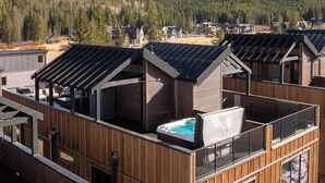Una cabaña moderna con fachada de madera y piscina en la azotea, rodeada de un bosque y montañas.