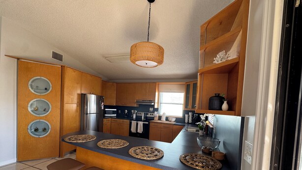 Eine moderne Küche mit Holzausstattung, einem Edelstahlkühlschrank, einer zentralen Kochinsel mit Sitzgelegenheiten und einer Hängelampe.