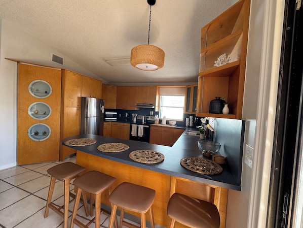 Una cocina moderna con armarios de madera, un refrigerador de acero inoxidable, una isla central con taburetes y una lámpara colgante.