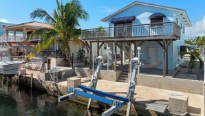 Ein Küsteneigentum mit Anlegesteg, Boot, zweistöckigem Haus mit Balkon und einer Palme.