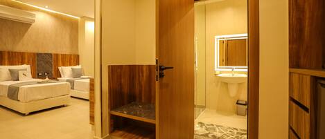 A modern hotel room with a wooden wardrobe, a bed with a headboard, a bedside table, and a bathroom with a sink and mirror.