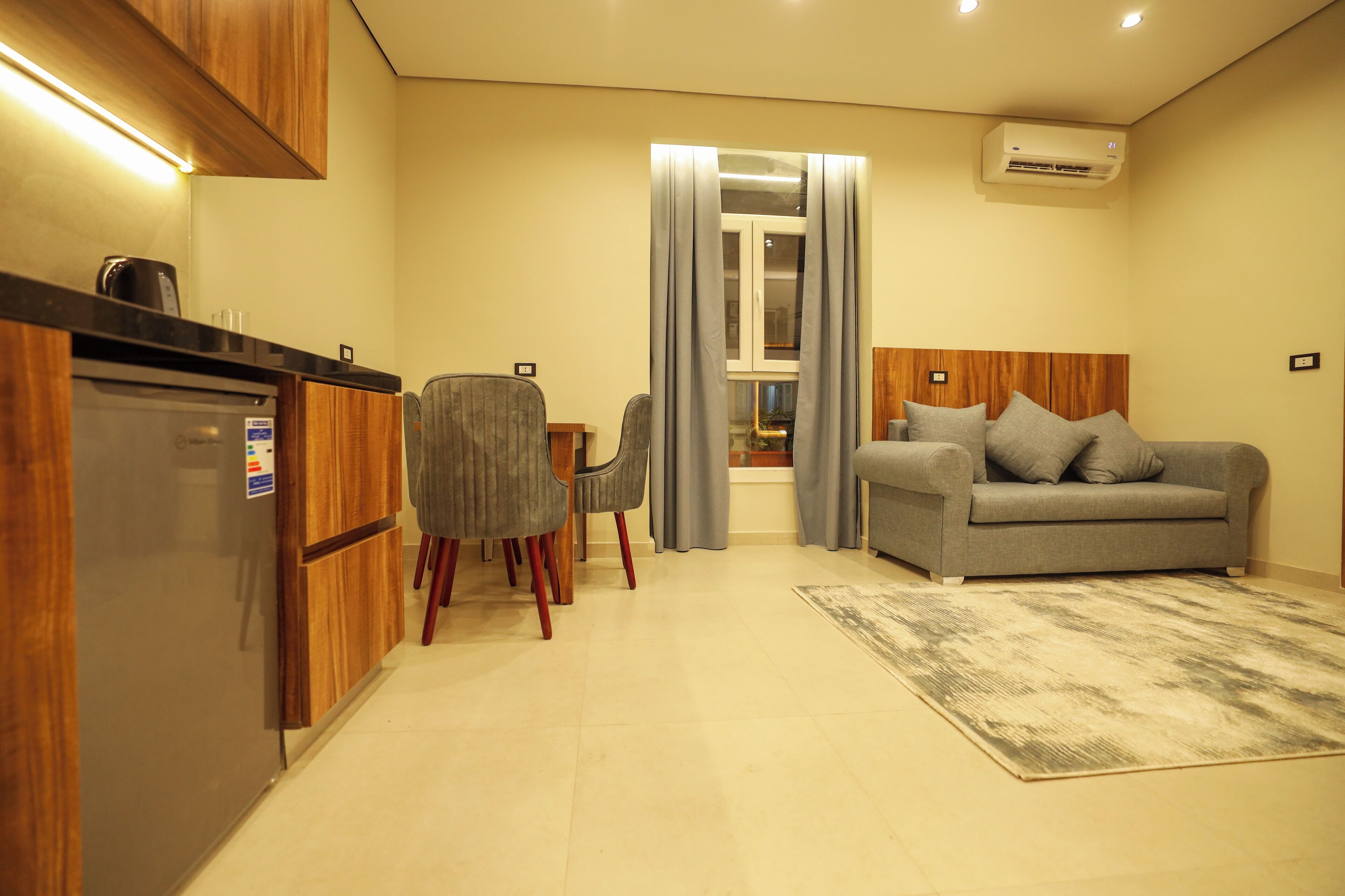 A modern living room with a grey sofa, wooden cabinets, and a tiled floor.