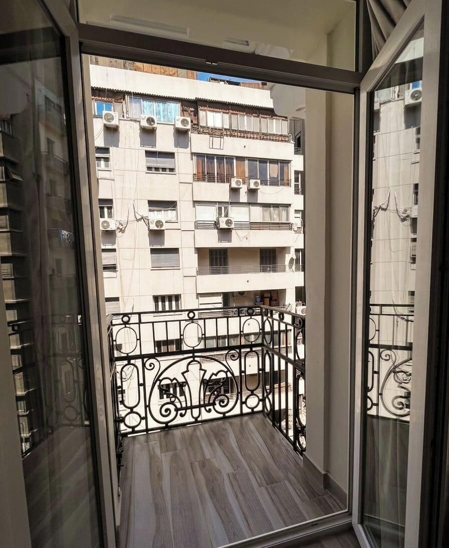 Un balcón con barandilla metálica y vistas a un edificio de varios pisos con balcones.