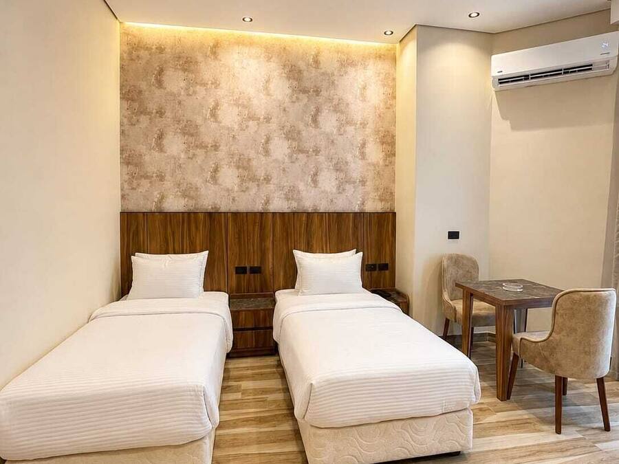 A hotel room with two beds, a wooden headboard, a small table with chairs, and an air conditioning unit.