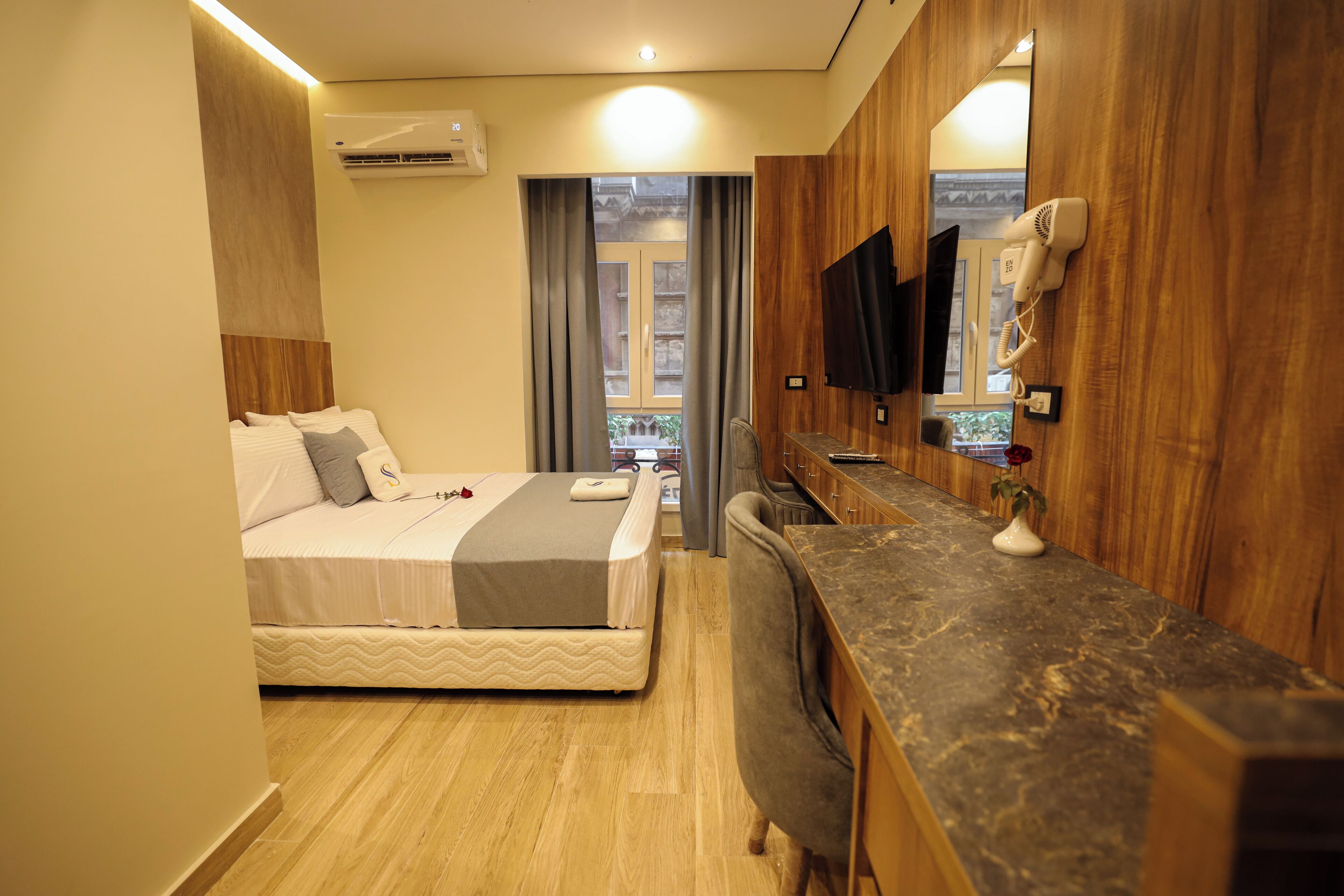A hotel room with a bed, a desk, a mirror, a hairdryer, and a view of the outside.