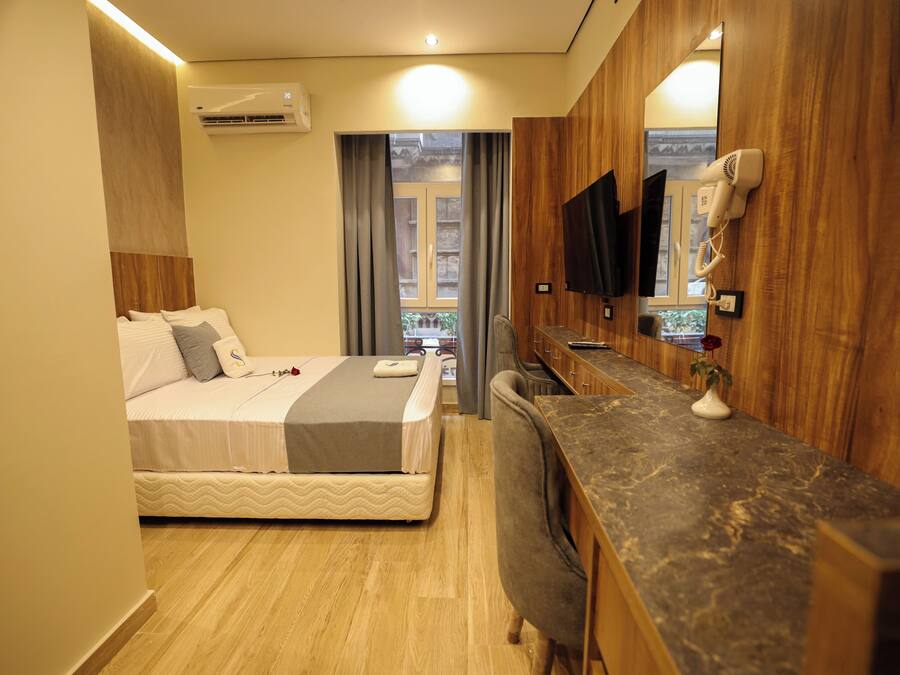A hotel room with a bed, a desk, a mirror, a hairdryer, and a view of the outside.