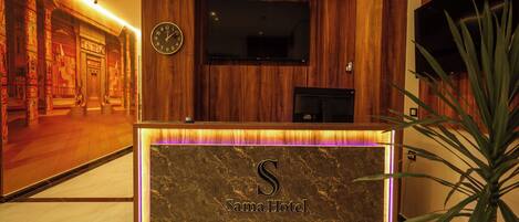 Ein Empfangsschalter mit Marmorplatte und leuchtendem 'Sama Hotel'-Schild.