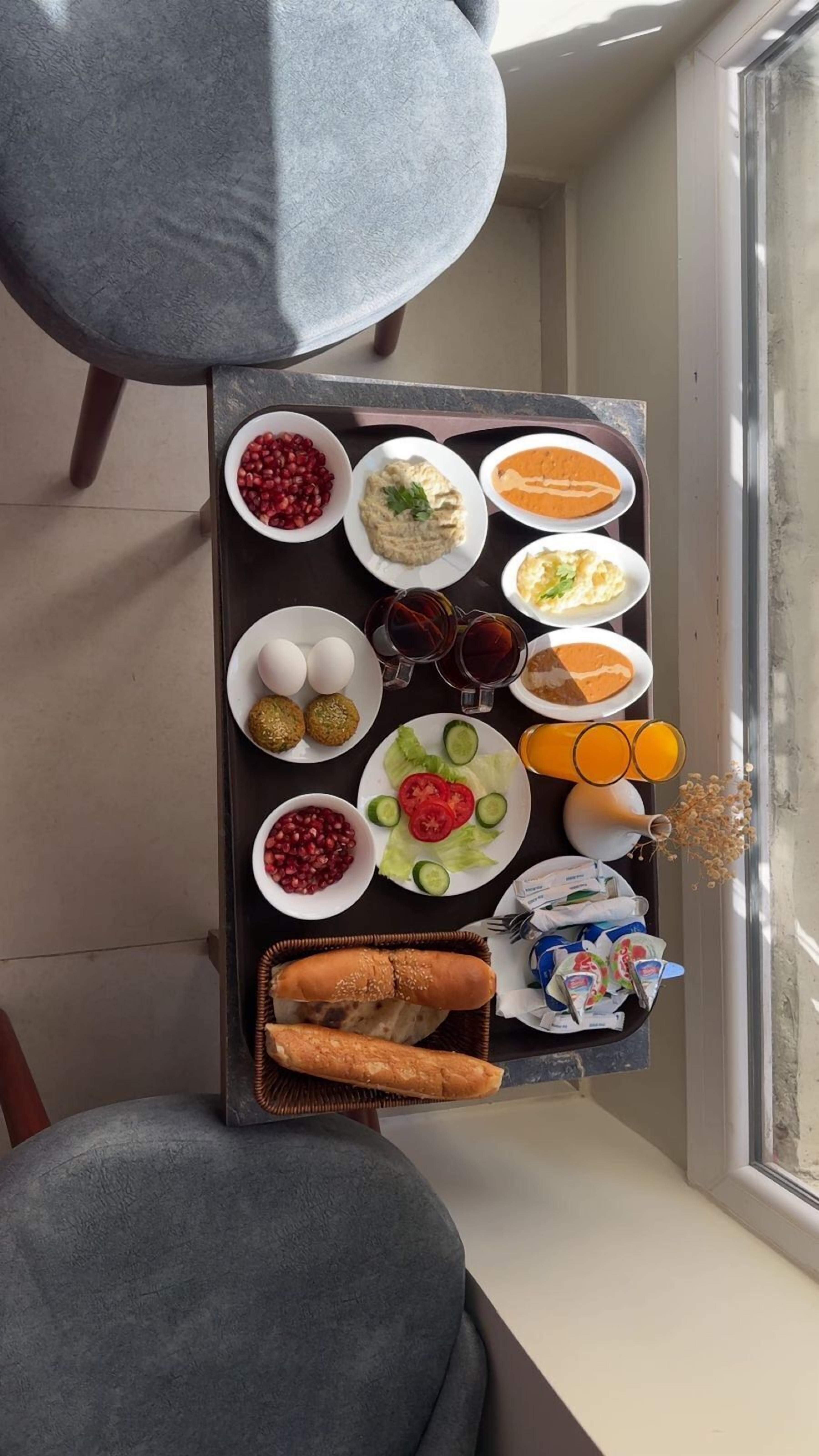 A tray with various food items including pomegranate seeds, hummus, falafel, eggs, and bread, placed on a windowsill.