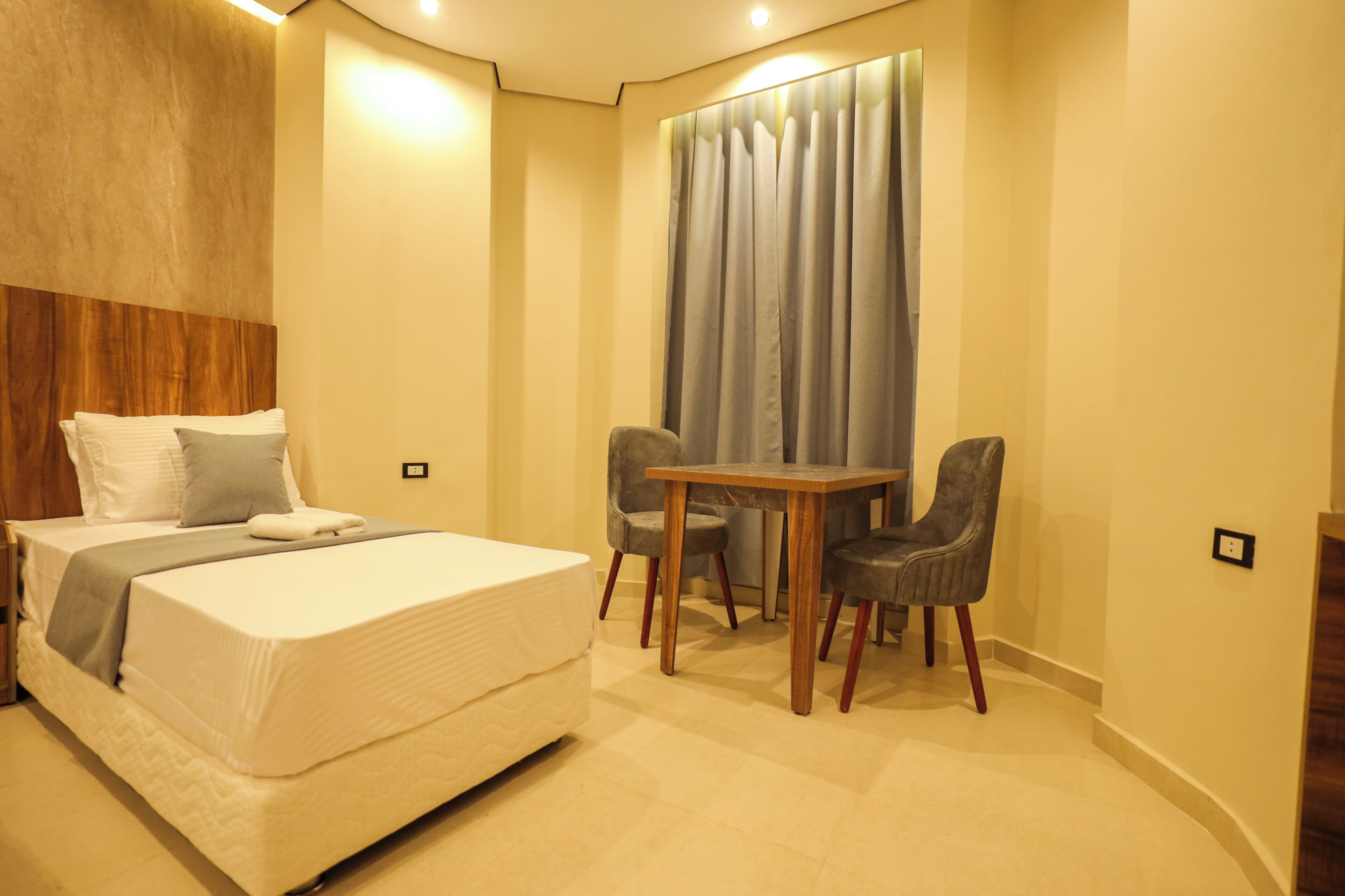 Una habitación de hotel con una cama, una mesa, dos sillas y un ventanal con cortinas.