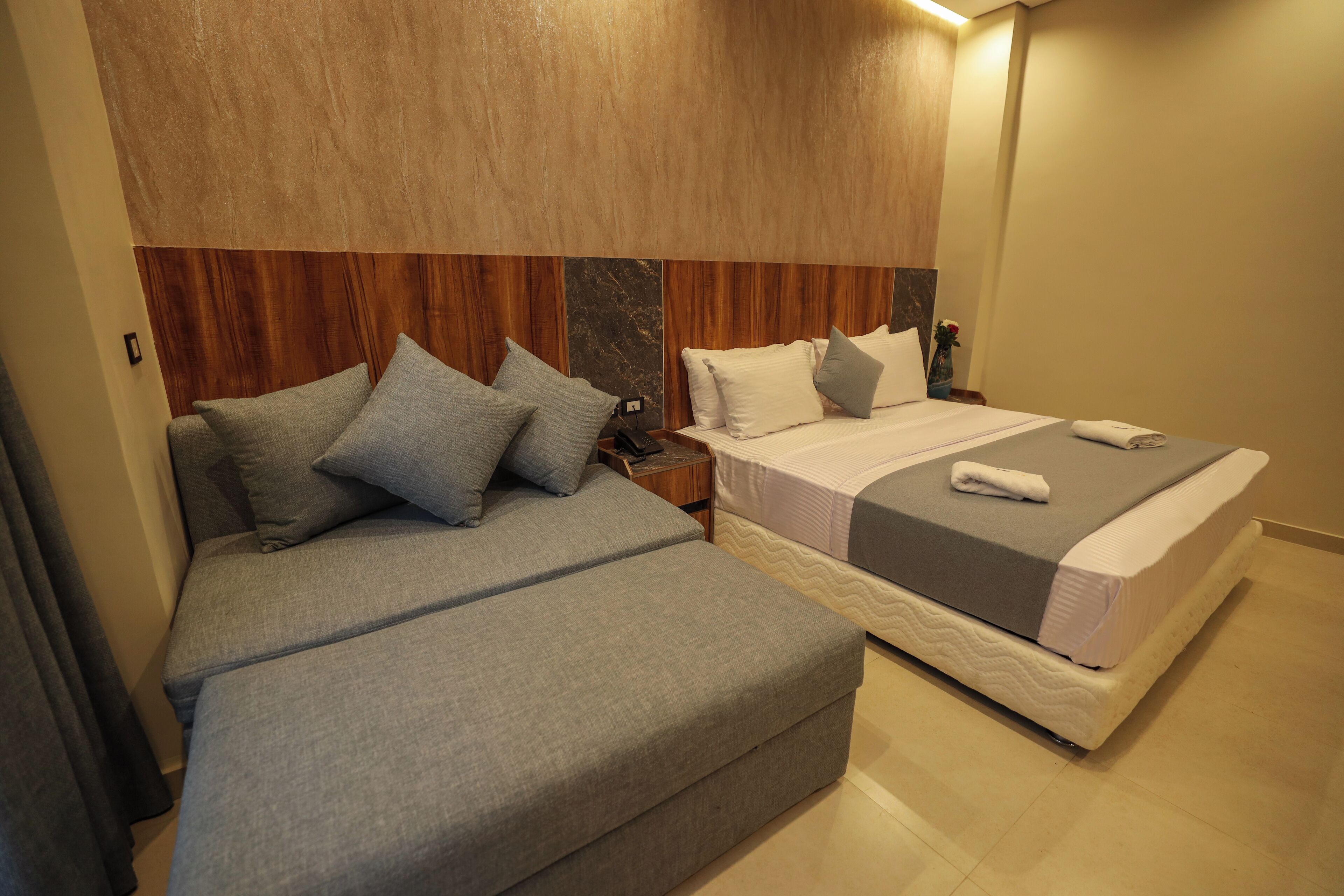 Habitación de hotel con dos camas, cabecero de madera y una mesita de noche con lámpara.
