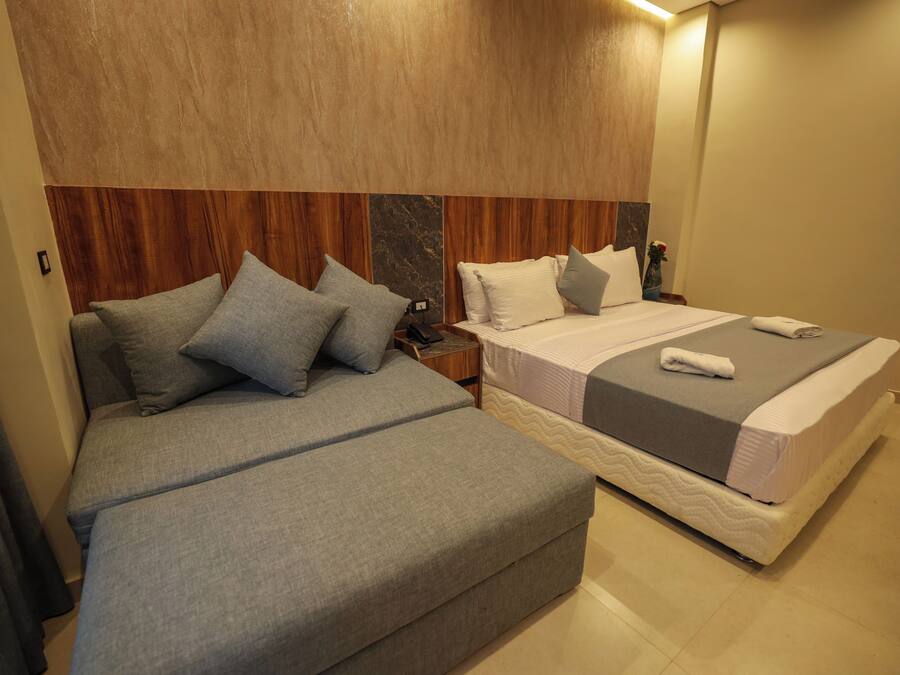 Habitación de hotel con dos camas, cabecero de madera y una mesita de noche con lámpara.