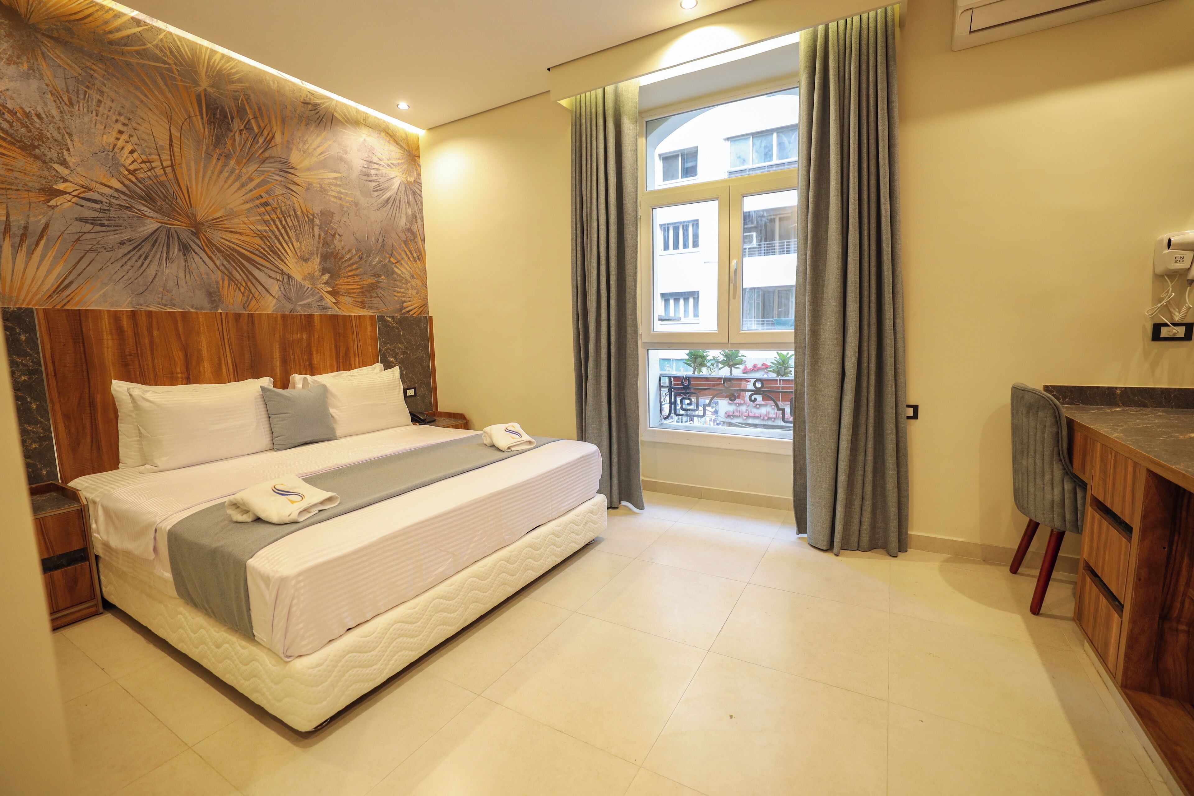Camera d'albergo con un letto grande, una testiera in legno, un comodino, una piccola scrivania e una finestra con tende.