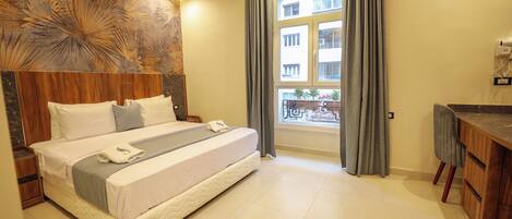Camera d'albergo con un letto grande, una testiera in legno, un comodino, una piccola scrivania e una finestra con tende.