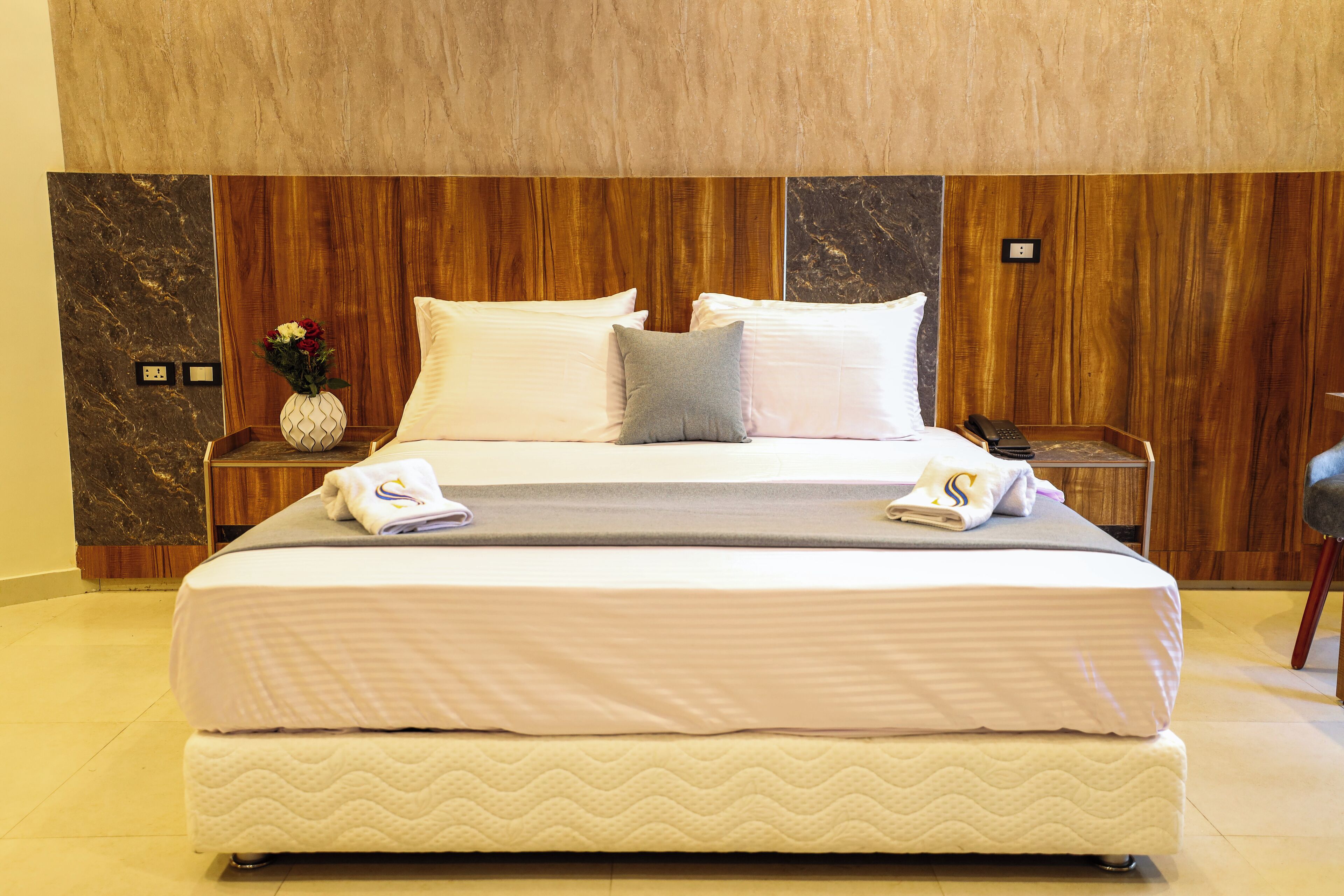 A neatly made bed with white linens, a grey pillow, and a small vase with flowers on the nightstand beside it.