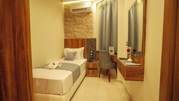 A hotel room with a bed, nightstand, chair, desk, mirror, and a wall-mounted air conditioner.