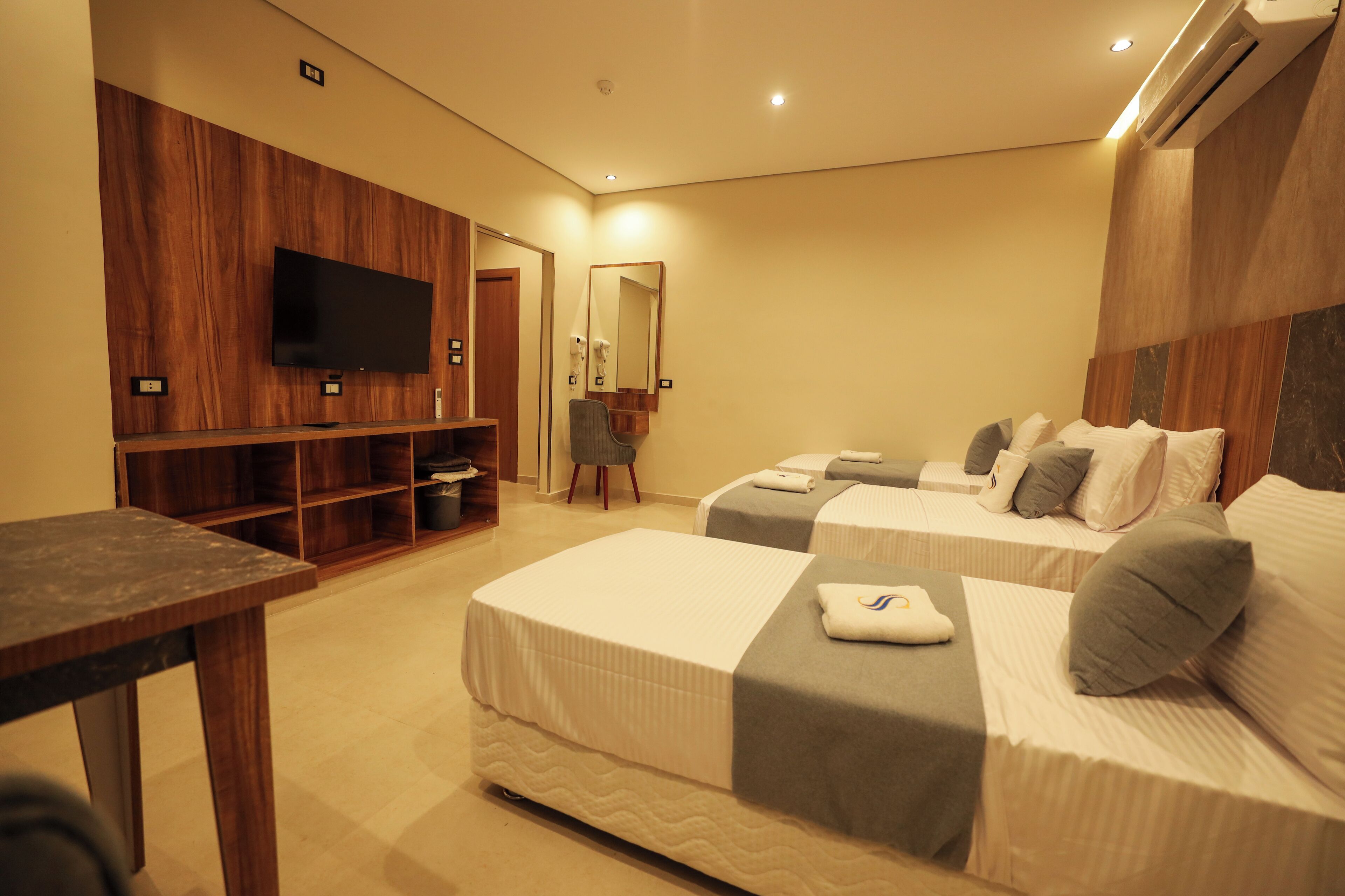 A hotel room with two beds, a TV, a mirror, and a wooden panel wall.