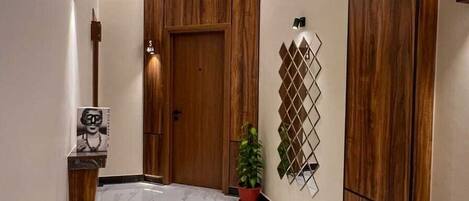 A hallway with a wooden door, a potted plant, and a wall-mounted decorative piece.