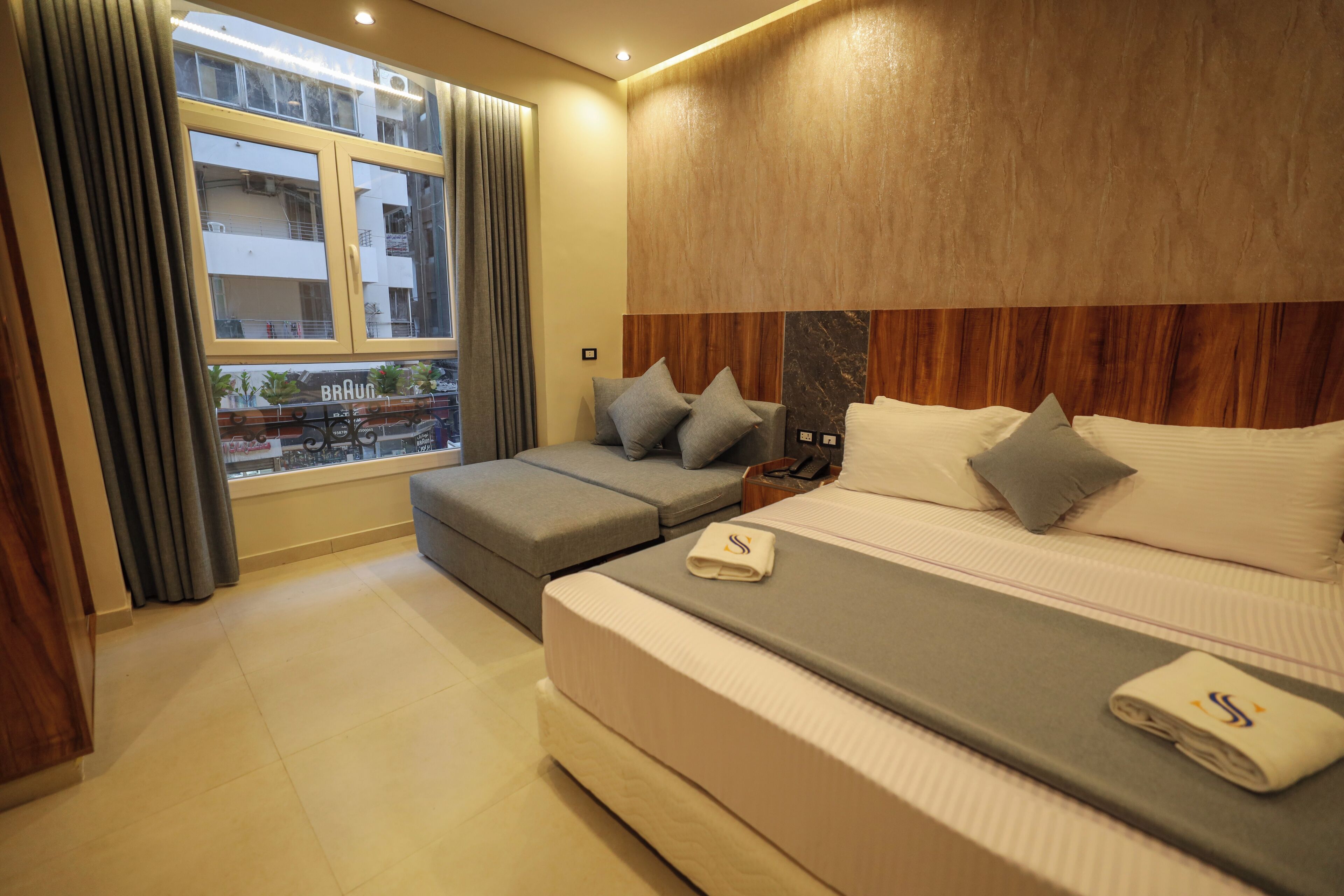 Ein modernes Hotelzimmer mit einem großen Bett, einer Couch und Blick auf ein Gebäude.