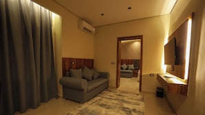 A modern hotel room with a sofa, a flat-screen TV, a wooden headboard, and a large window with curtains.
