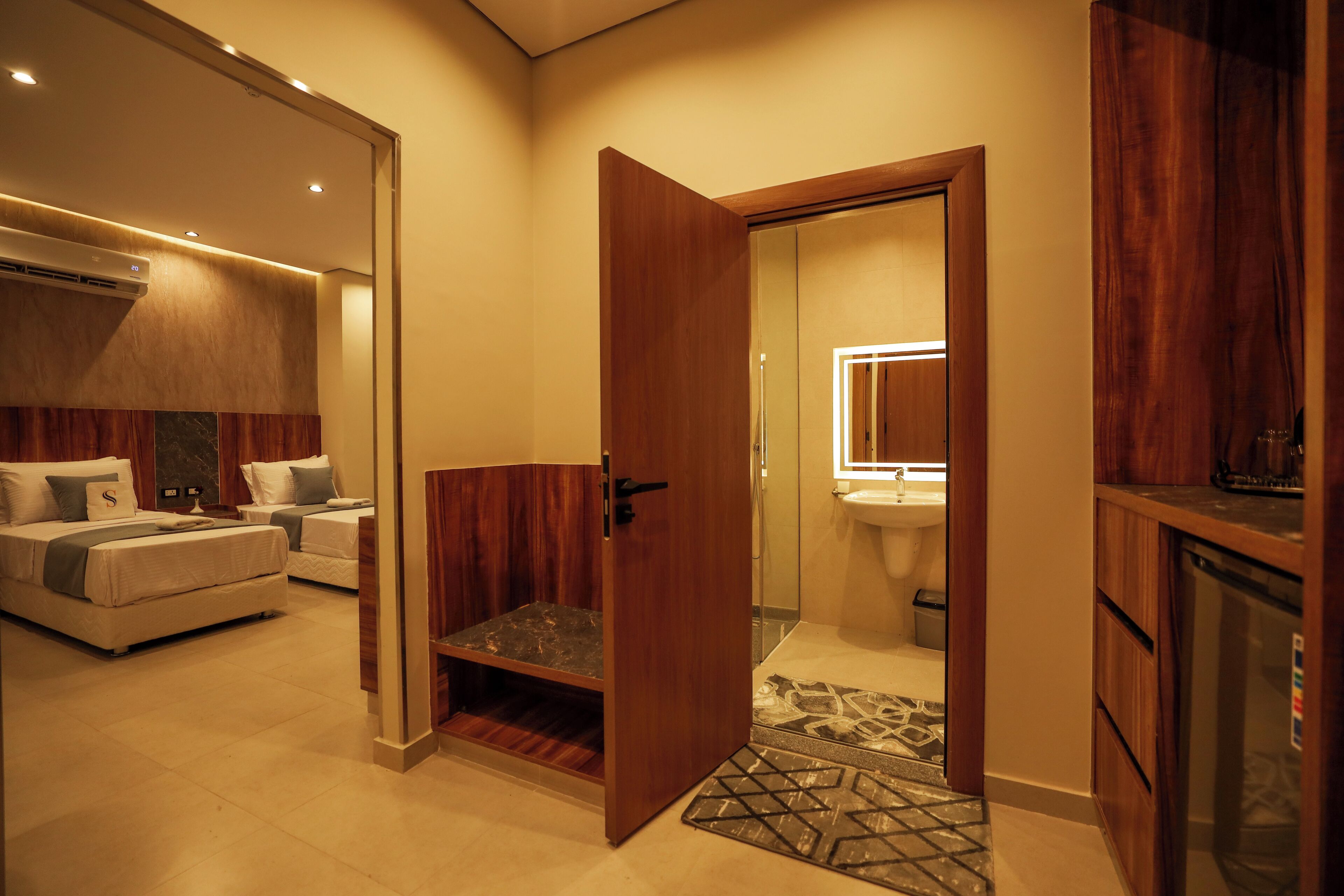 Una habitación de hotel con una cama, un pequeño rincón de descanso, una puerta de madera y un baño con lavabo y espejo.