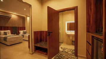 Una habitación de hotel con una cama, un pequeño rincón de descanso, una puerta de madera y un baño con lavabo y espejo.