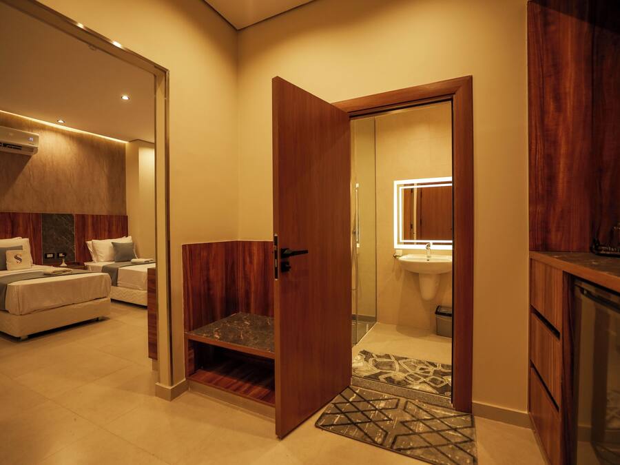 Una habitación de hotel con una cama, un pequeño rincón de descanso, una puerta de madera y un baño con lavabo y espejo.