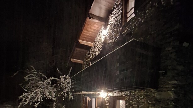 Ein Steinhaus mit geneigtem Dach und einer Holztür. Schnee liegt auf dem Boden und um das Gebäude herum.