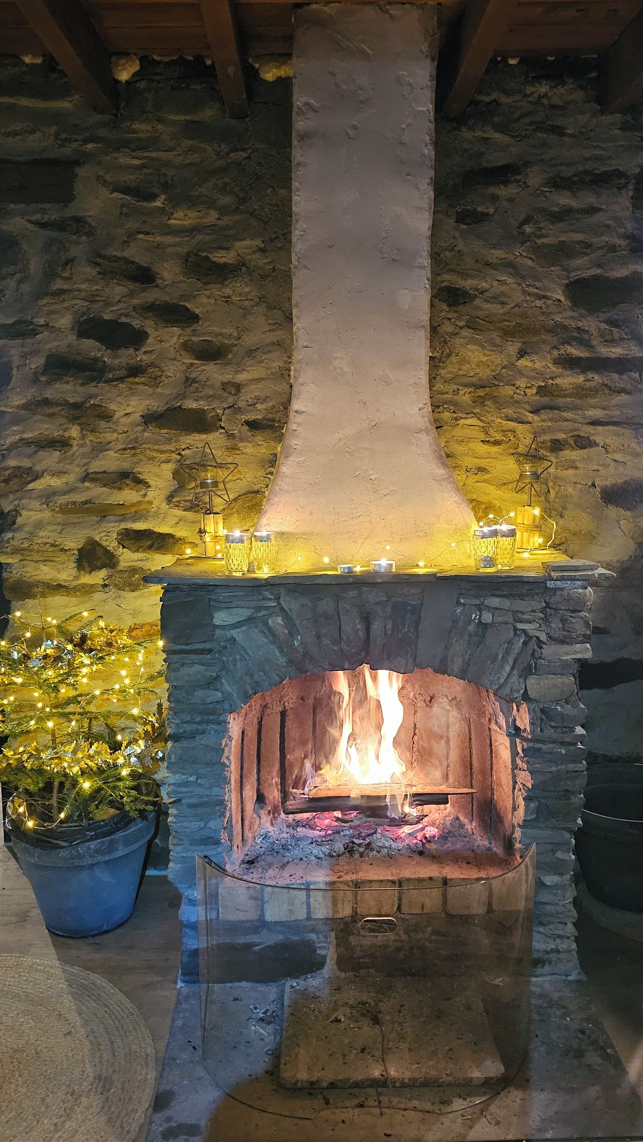 A stone fireplace with a fire burning inside, surrounded by stone walls and a wooden ceiling.