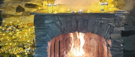 A stone fireplace with a fire burning inside, surrounded by stone walls and a wooden ceiling.