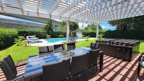 Eine Außenpatio mit einem Glastisch, Korbstühlen, einem Pool und einer Pergola.