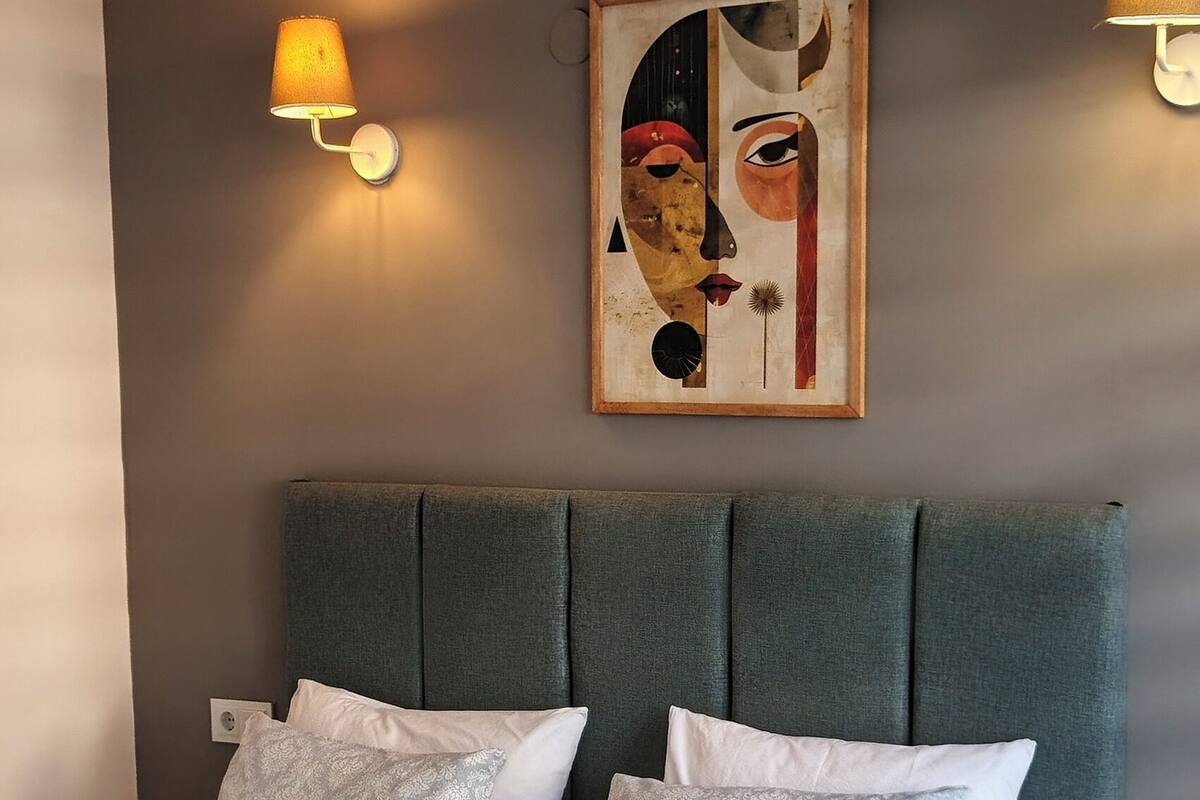 A modern bedroom with a large bed, grey headboard, and two wall-mounted lamps.