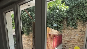 Ein Zimmer mit einer Schiebetür, die auf eine Terrasse mit rotem Zaun, Steinmauer und gelbem Stuhl führt.
